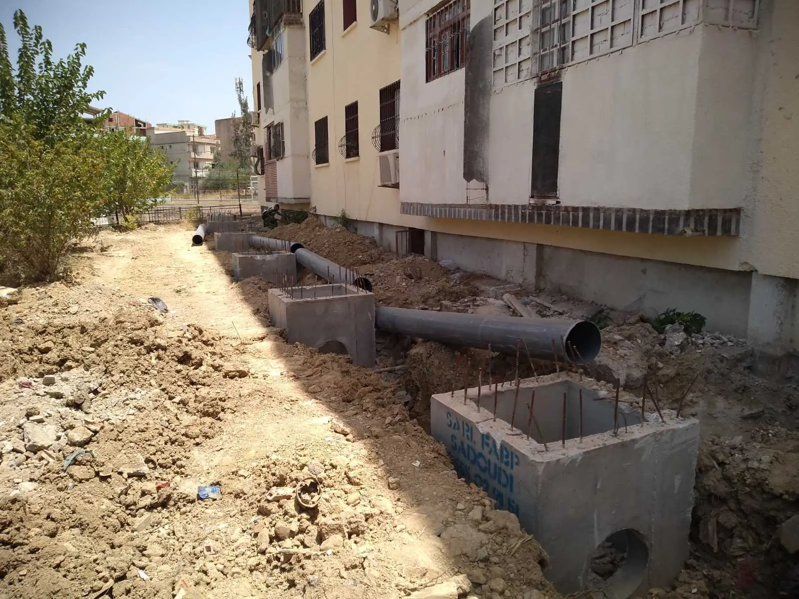 Réseau en cours de pose au pied d'un immeuble, avec des regards en béton